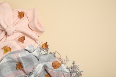 Sweater, scarf and dry leaves on beige background, flat lay with space for text. Autumn season