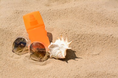 Bottle with sun protection spray, sunglasses and seashell on sandy beach, space for text