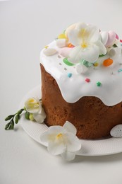 Photo of Traditional Easter cake with sprinkles, jelly beans, marshmallows, flowers and decorated egg on white table, closeup