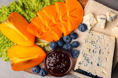 Photo of Delicious persimmon, blue cheese, blueberries and jam served on light grey table, flat lay