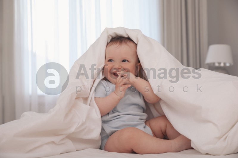 Cute little baby under soft blanket on bed at home