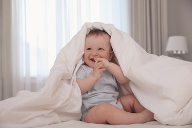 Cute little baby under soft blanket on bed at home