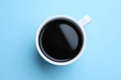 White mug of freshly brewed hot coffee on light blue background, top view