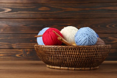 Wicker basket with clews of colorful knitting threads and crochet hooks on wooden table