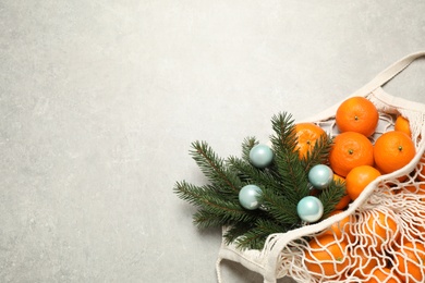 Photo of Christmas composition with fresh tangerines in mesh bag on light background, flat lay. Space for text