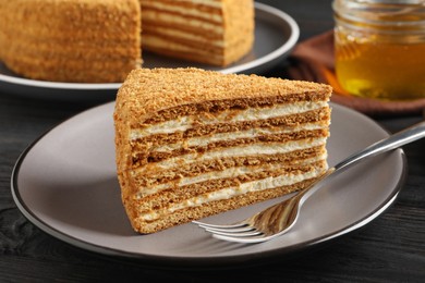 Slice of delicious layered honey cake served on black wooden table, closeup