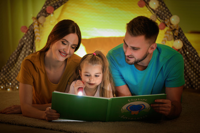 Family with flashlight reading book at home