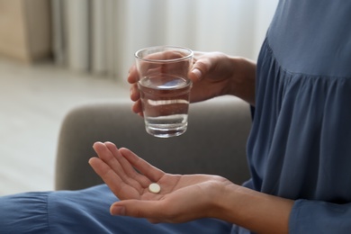 Woman holding glass of water and pill at home, closeup