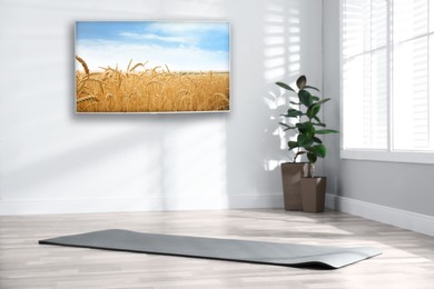 Modern wide screen TV on white wall in room with yoga mat