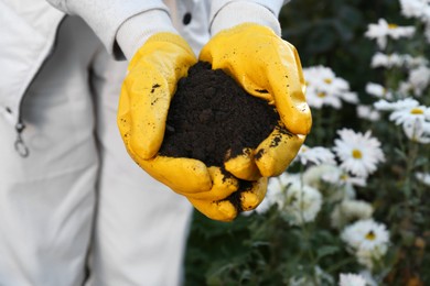 Photo of Woman in gardening gloves holding pile of soil outdoors, closeup