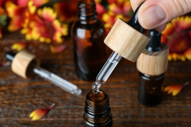 Woman pouring essential oil from pipette into bottle on wooden table, closeup