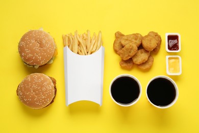 Different fast food on yellow background, flat lay