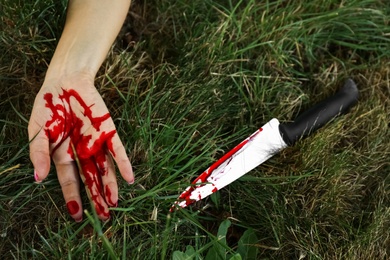 Crime scene with dead woman's body and bloody knife on green grass outdoors, closeup. Detective case