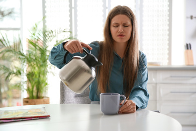 Sleepy young woman pouring coffee into cup at home in morning
