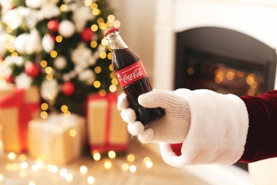 MYKOLAIV, UKRAINE - JANUARY 18, 2021: Santa Claus holding Coca-Cola bottle in room decorated for Christmas, closeup