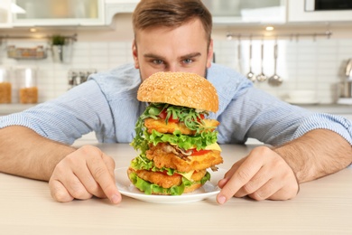 Photo of Young hungry man and huge burger in kitchen
