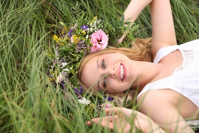 Young woman wearing wreath made of beautiful flowers on green grass