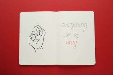 Photo of Notebook with phrase Everything Will Be Okay and drawing of hand showing gesture on red background, top view