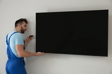 Professional technician with screwdriver installing modern flat screen TV on wall indoors