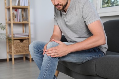 Photo of Man suffering from knee pain on sofa indoors, closeup