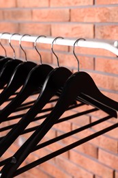 Black clothes hangers on rack near red brick wall, closeup