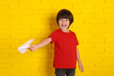 Cute little boy with paper plane near yellow brick wall