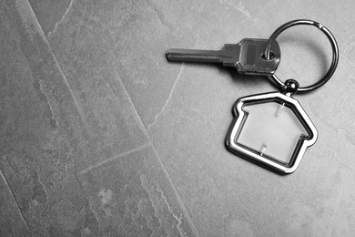 Key with trinket in shape of house on grey stone background, top view and space for text. Real estate agent services