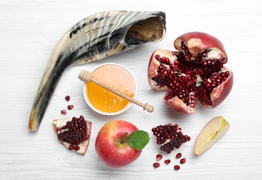 Honey, pomegranate, apples and shofar on white wooden table, flat lay. Rosh Hashana holiday
