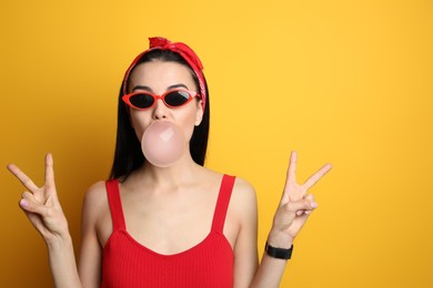 Photo of Fashionable young woman in pin up outfit blowing bubblegum on yellow background, space for text