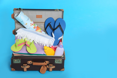 Packed vintage suitcase with different beach objects on light blue background, space for text. Summer vacation