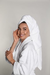 Photo of Beautiful young woman wearing bathrobe and towel on head against light background