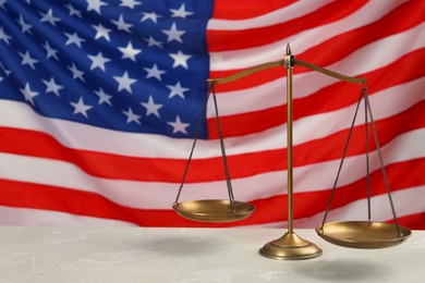 Scales of justice on light grey table against American flag. Space for text