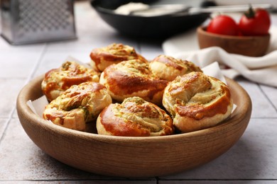 Photo of Fresh delicious puff pastry with tasty filling in wooden bowl on white tiled surface, closeup