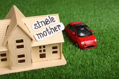 House model, toy car and text Single Mother on green grass