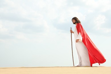 Jesus Christ walking with stick in desert. Space for text