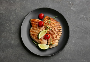 Tasty grilled chicken fillets with tomatoes, lime slices and green sprouts on grey table, top view