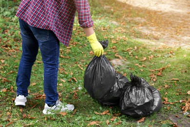 Photo of Man holding plastic bags with garbage in park, closeup.