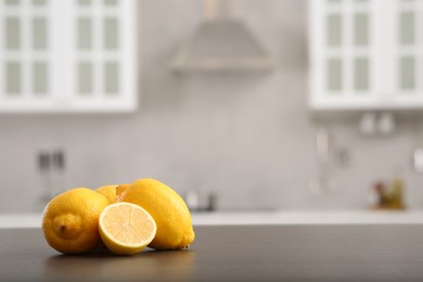 Photo of Whole and cut lemons on wooden counter in kitchen, space for text