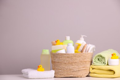 Photo of Wicker basket with baby cosmetic products, bath accessories and rubber ducks on white table against grey background. Space for text