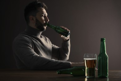 Addicted man drinking alcohol at wooden table indoors, focus on glass of beer