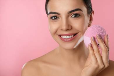 Young woman holding facial cleansing brush on pink background, closeup. Washing accessory