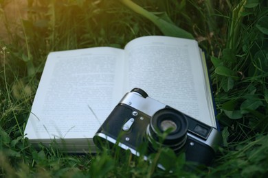 Open book and vintage camera on green grass outdoors