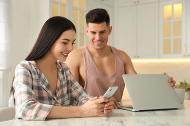 Photo of Happy couple wearing pyjamas with gadgets spending time together in kitchen