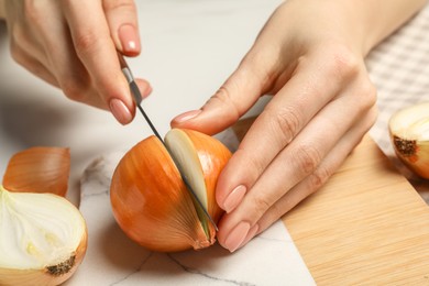 Photo of Woman cutting ripe onion at white table, closeup