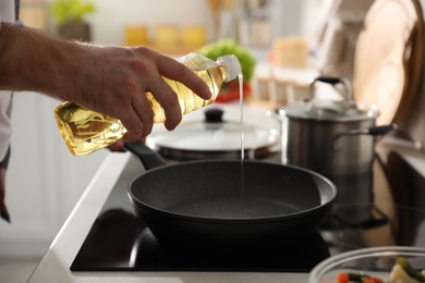 Man pouring cooking oil into frying pan in kitchen, closeup