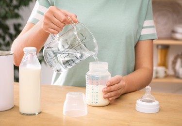 Woman preparing infant formula at table indoors, closeup. Baby milk