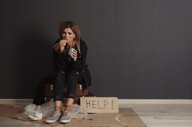 Poor homeless woman with bread and mug asking for help near dark wall. Space for text