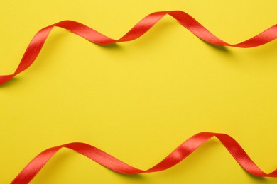 Photo of Beautiful red ribbons on yellow background, flat lay. Space for text