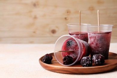 Tasty blackberry ice pops in plastic cups on white table, space for text. Fruit popsicle