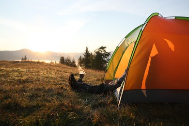 Man inside camping tent in mountains at sunset